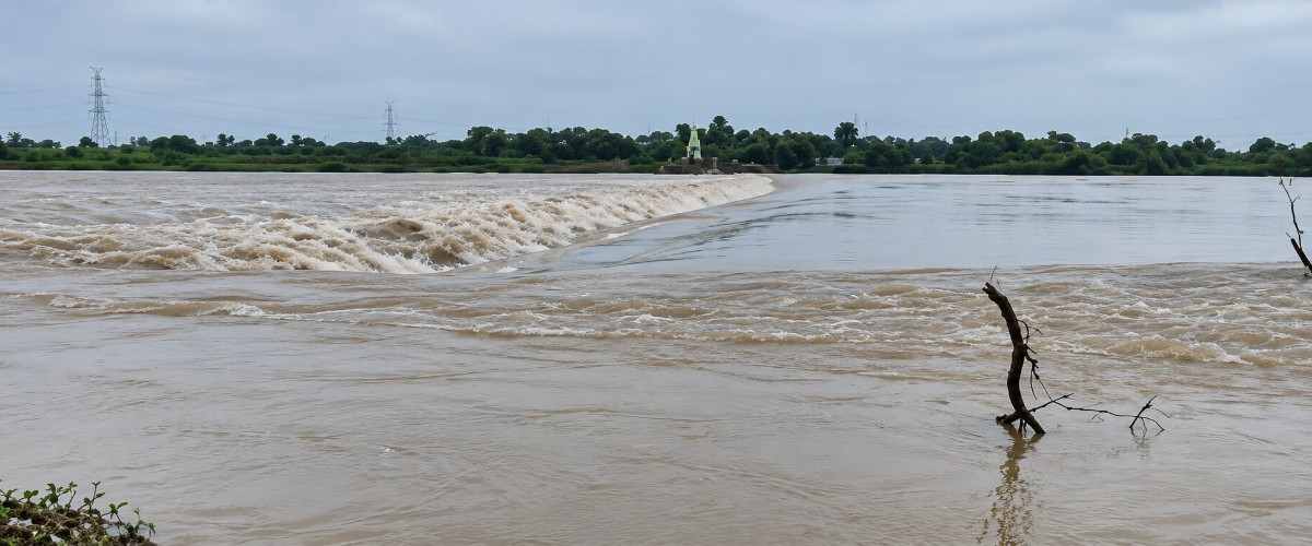 मुसळधार पावसानंतर बंधाऱ्यावरून वेगाने वाहणारे नदीचे पाणी